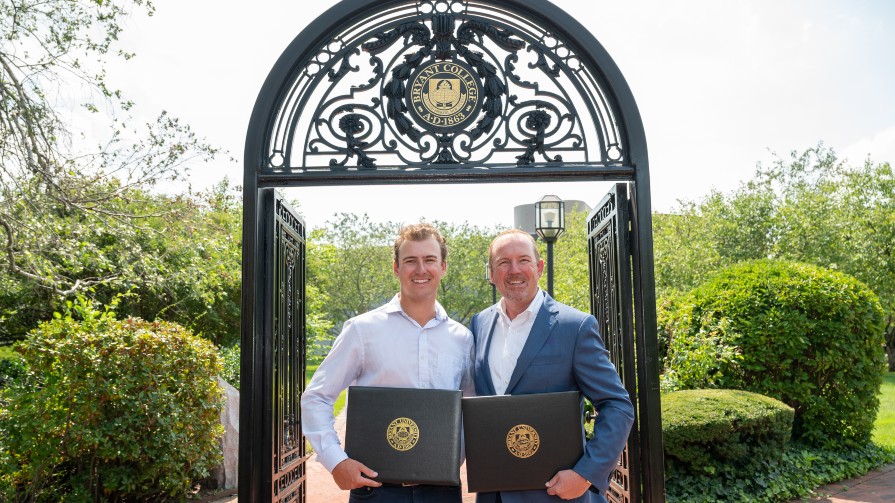 Dane ’23 and Brad Caron ’87, P’23 stand under the arch on Bryant's campus with their diplomas.